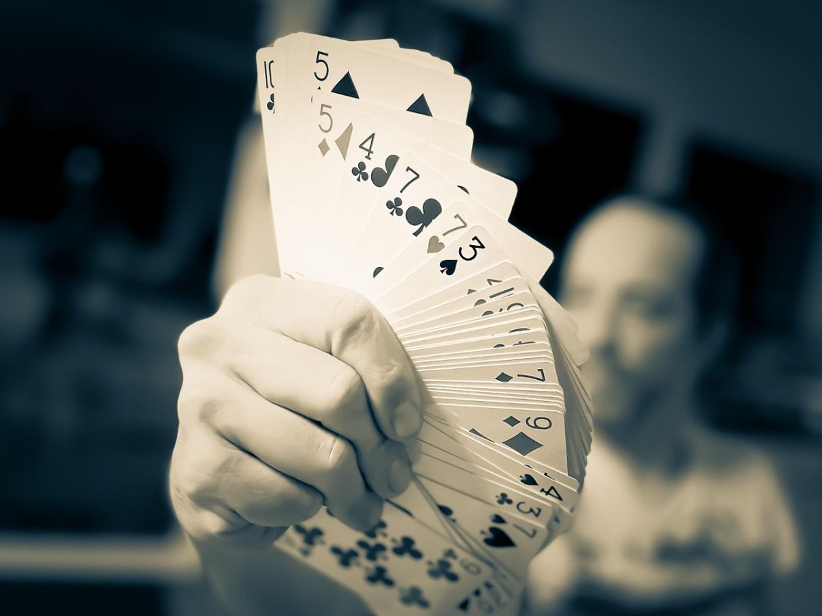 Main tenant un éventail de cartes de poker, illustrant le lancement du podcast Fade Us Sports par Phil Hellmuth sur le poker et les paris sportifs