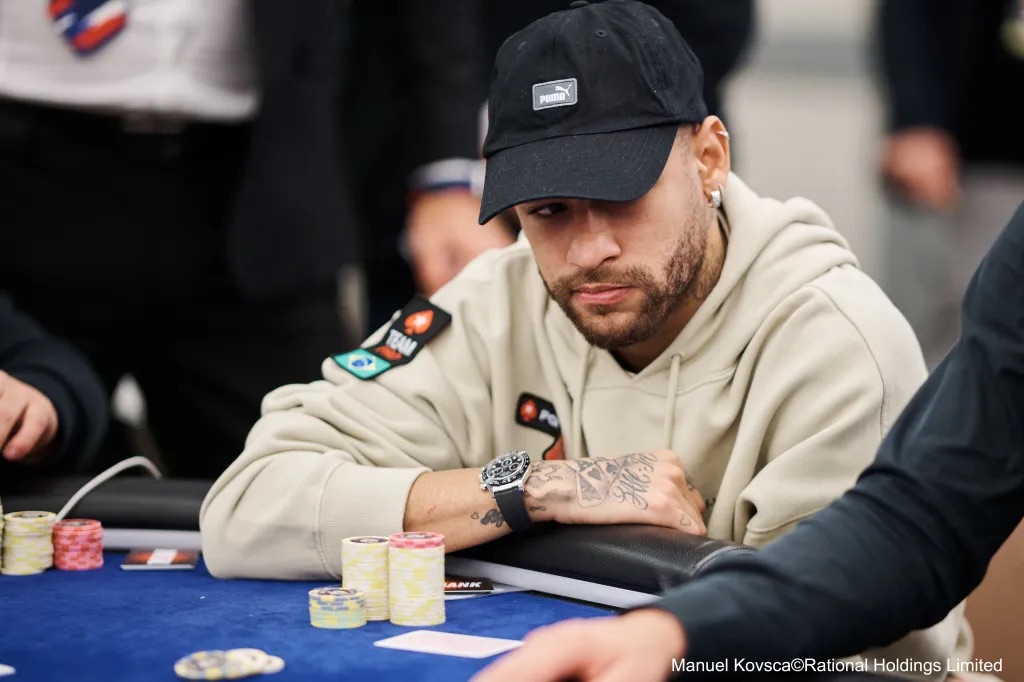 Neymar, joueur de football en tenue décontractée concentré à une table de poker, jetons empilés devant lui