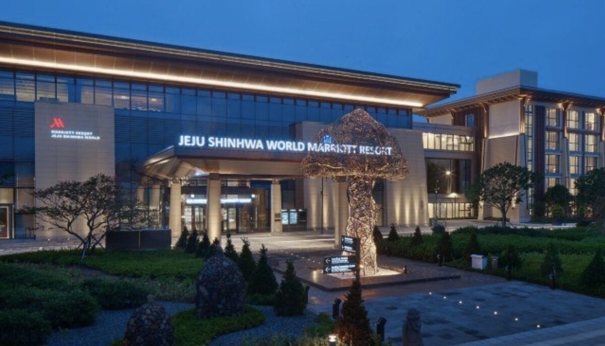 제주 신화월드 리조트 정문 전경, 입구에 'JEJU SHINHWA WORLD SHINHWA RESORT' 간판이 보이며 주변에 나무와 차량이 있는 모습.