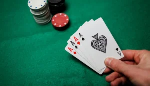 Bild på en hand som håller upp fyrtal i ess på ett pokerbord med marker i bakgrunden