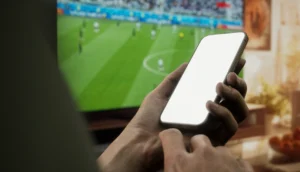 Person använder mobilen medan en fotbollsmatch visas på tv.