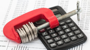 A red clamp puts the squeeze on a stack of coins. Calculator, tax documents.