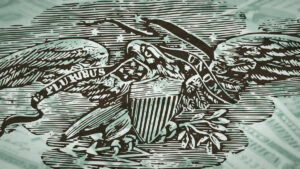 A woodcut of an American eagle bearing a banner reading "E Pluribus Unum," overlaid on a blurred image of US currency.