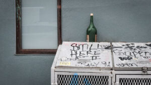Dingy New York street scene featuring bottle, window, and graffiti.