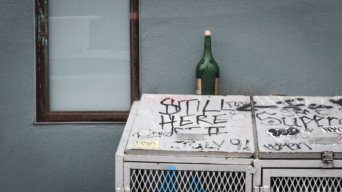 Dingy New York street scene featuring bottle, window, and graffiti.