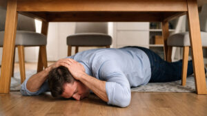 A man lies face down on the floor under a table.