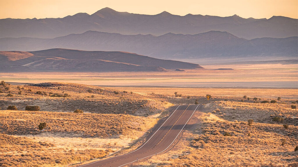 A Nevada desert highway crests a hill in the summer heat.
