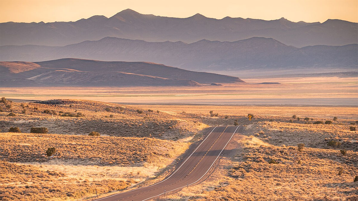 A Nevada desert highway crests a hill in the summer heat.