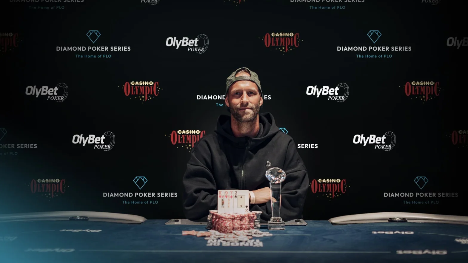 Jonas Kronwitter posing with a trophy and poker chips in front of a Diamond Poker Series backdrop