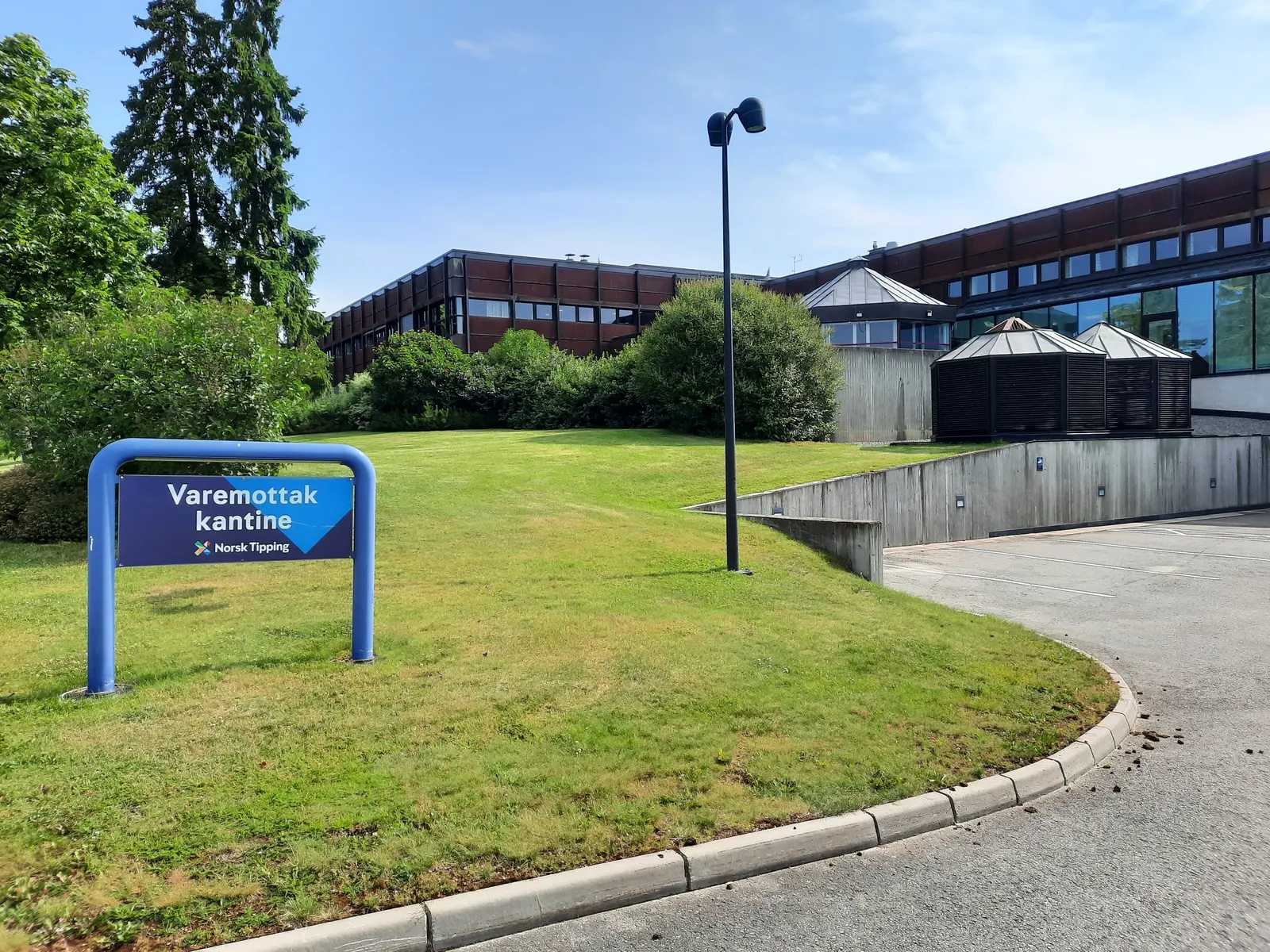 A sign for the goods reception and canteen at the Norsk Tipping facility with the office building in the background.